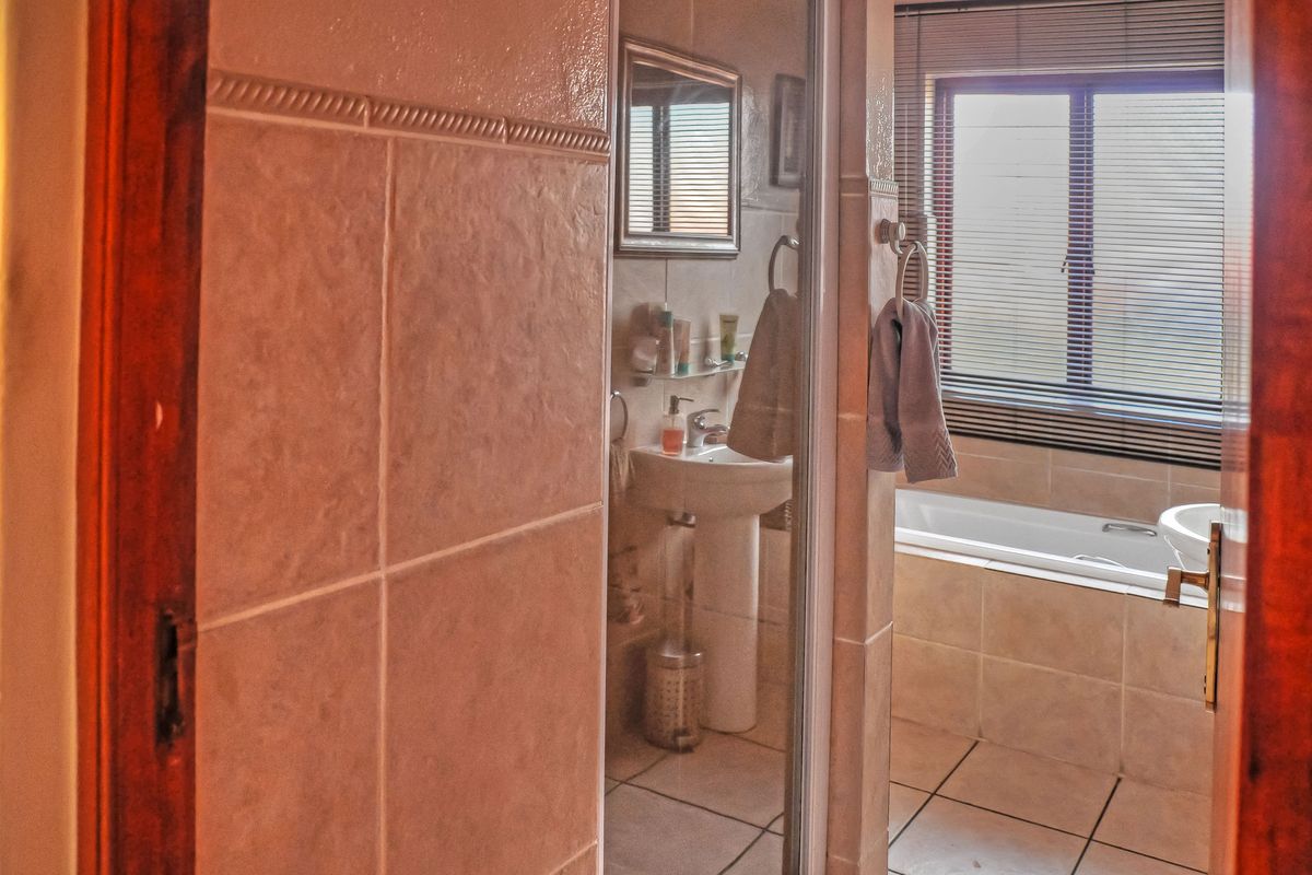 A functional bathroom featuring a pedestal basin, a built-in bathtub, and tiled finishes, offering a practical layout with natural light from the window.