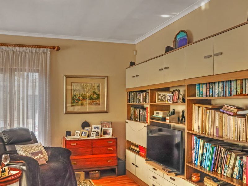 A living room featuring extensive built-in wall cabinetry, hardwood flooring, and natural light through a large window with curtain treatments.