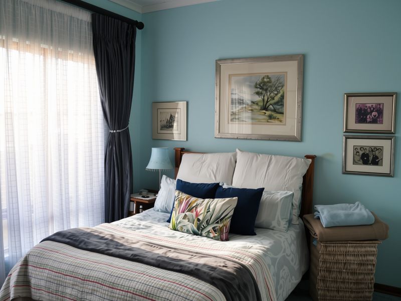 A well-maintained bedroom featuring light blue walls, a large window with layered curtains, and ample natural light.