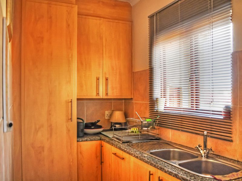 A functional kitchen featuring warm-toned laminate cabinetry, granite countertops, a double stainless steel sink, and a tiled backsplash with natural light from the window.