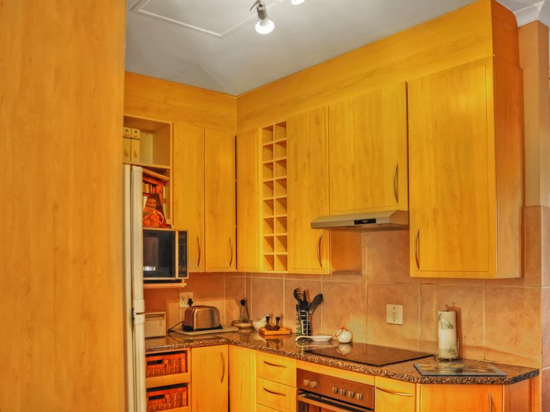 A functional kitchen featuring light wood-toned cabinetry, granite-look laminate countertops, a built-in oven, electric cooktop, and a tiled backsplash.