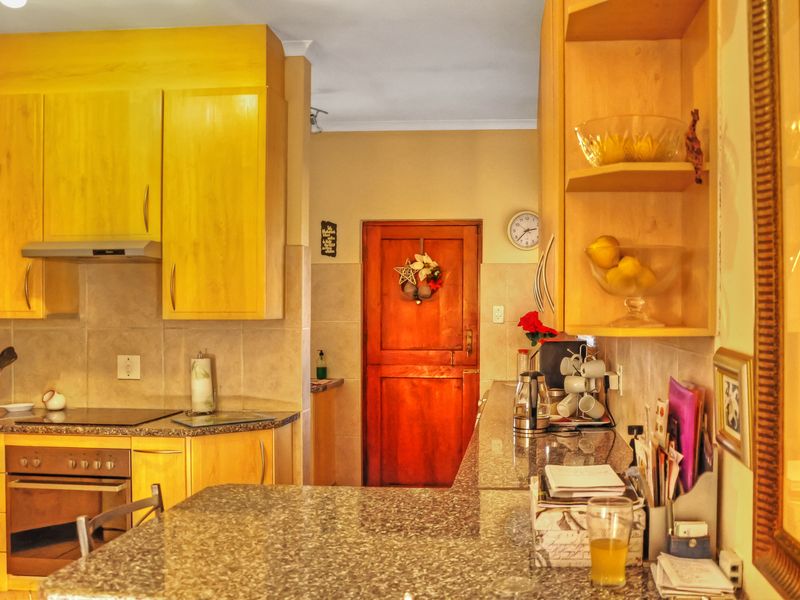 A functional kitchen featuring light wood cabinetry, granite countertops, and integrated appliances, leading to a solid wood door.