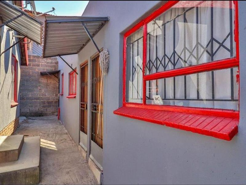A narrow exterior side passage featuring concrete pathways, metal security gates, and window bars with red painted frames.