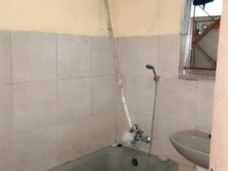 A dated bathroom featuring a bathtub, handheld shower, and pedestal basin, requiring cosmetic updates and modernization of fixtures.