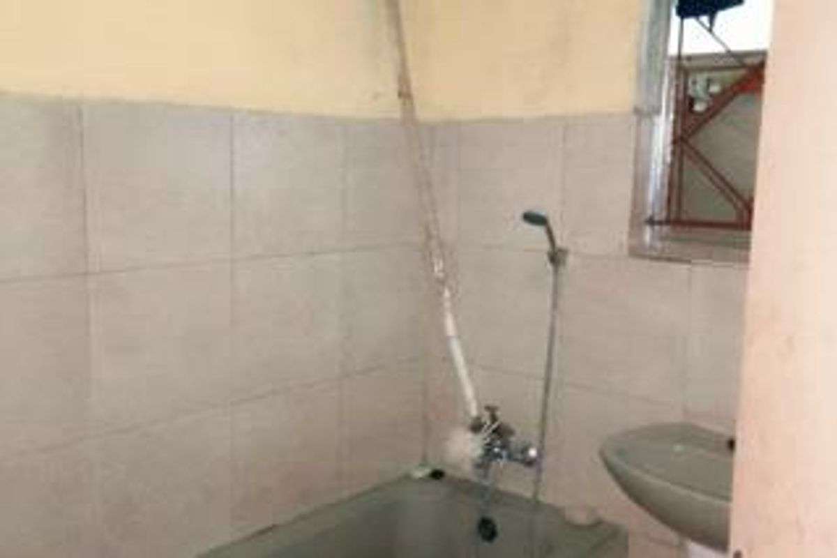 A dated bathroom featuring a bathtub, handheld shower, and pedestal basin, requiring cosmetic updates and modernization of fixtures.