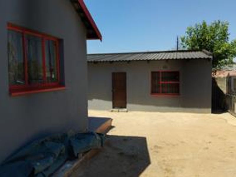 Rear exterior view of the property featuring grey painted walls, red steel window frames, and a metal roof with a concrete yard area.