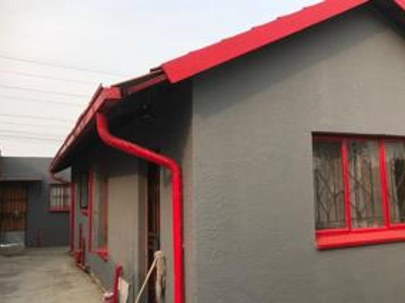Side view of the property featuring grey exterior walls with contrasting red window frames, gutters, and downpipes, set over a concrete paved area.