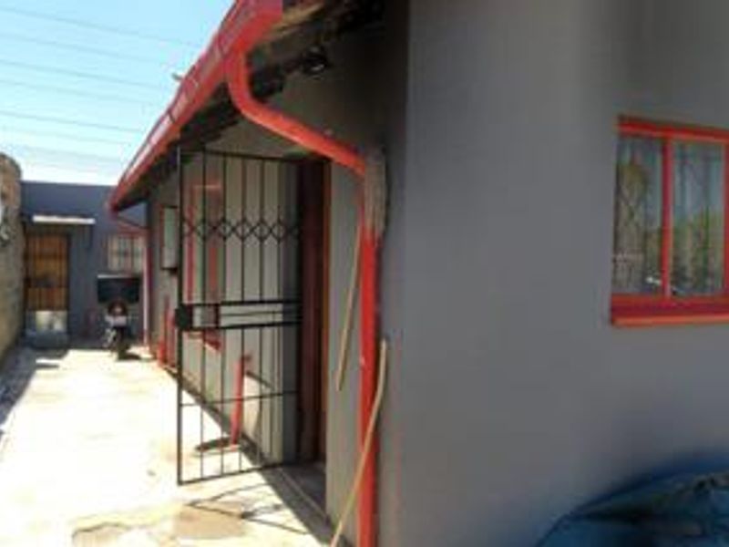 Side view of the property showing a concrete pathway, security gate, and exterior wall with painted window frames and guttering.