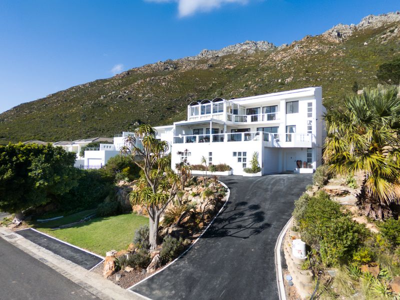 A multi-level residential property featuring a paved driveway, landscaped garden, and multiple balconies, set against a scenic mountain backdrop.