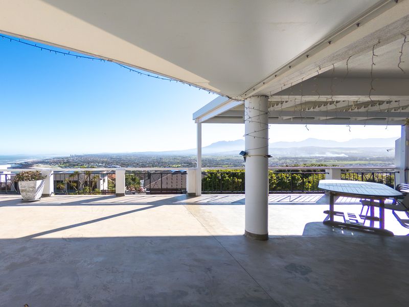 Spacious covered patio featuring concrete flooring and metal railings, offering expansive panoramic views of the surrounding landscape and coastline.