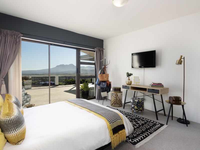 A well-lit bedroom featuring carpeted flooring, a wall-mounted television, and large sliding glass doors that open onto a balcony with scenic mountain views.