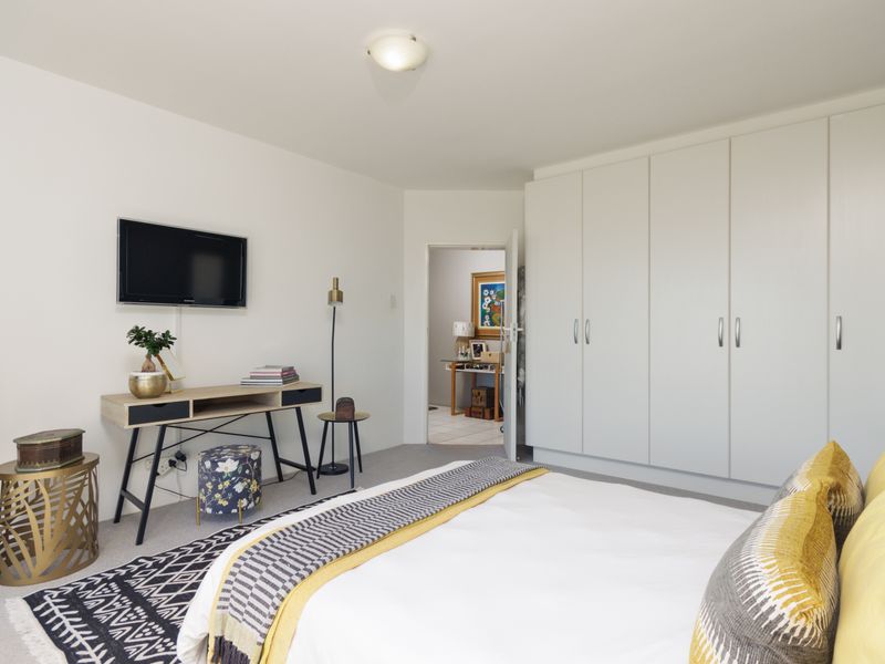 A well-maintained bedroom featuring neutral walls, carpeted flooring, and extensive built-in cupboard storage with a clean, modern aesthetic.