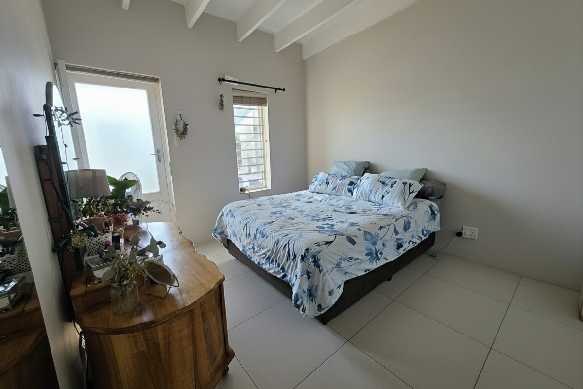 A bedroom featuring exposed white ceiling beams, large format floor tiles, and direct access to an outdoor area via a glass panel door.