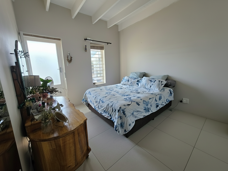 A bedroom featuring exposed white ceiling beams, large format floor tiles, and direct access to an outdoor area via a glass panel door.