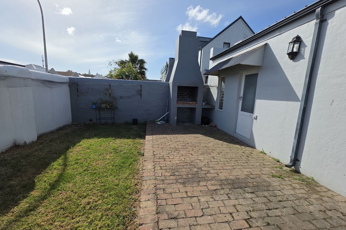 Rear courtyard featuring a brick paved patio, built-in braai, and boundary wall, offering a functional outdoor entertainment space.