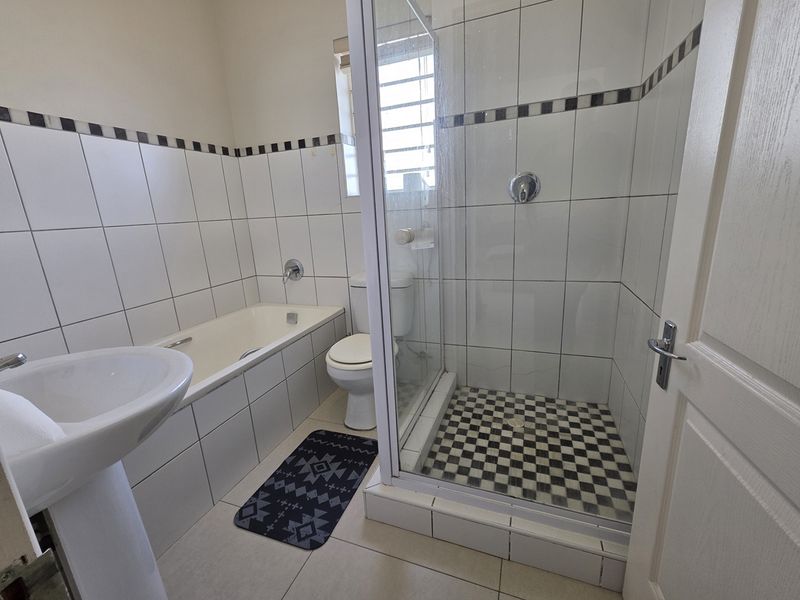 A functional bathroom featuring a pedestal basin, built-in bathtub, and a separate shower enclosure with tiled finishes.