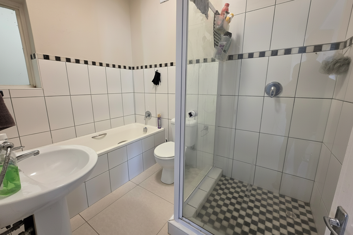 A functional bathroom featuring a pedestal basin, built-in bathtub, and a separate shower enclosure with tiled finishes throughout.