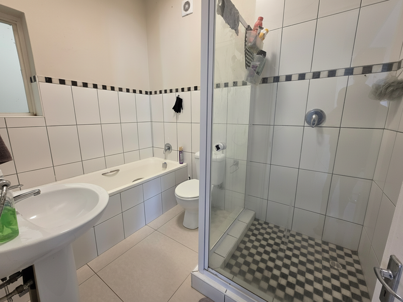 A functional bathroom featuring a pedestal basin, built-in bathtub, and a separate shower enclosure with tiled finishes throughout.