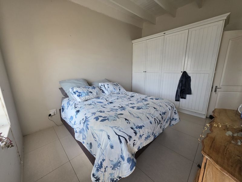 A bedroom featuring tiled flooring, exposed beam ceilings, and a large white built-in wardrobe.