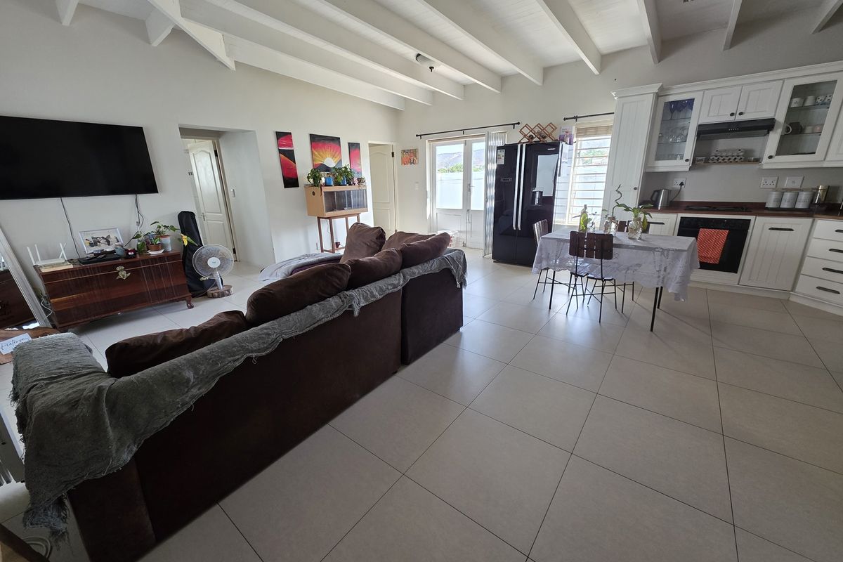 Spacious open-plan living and kitchen area featuring exposed beam ceilings, neutral tiled flooring, and a functional kitchen with built-in cabinetry and integrated appliances.