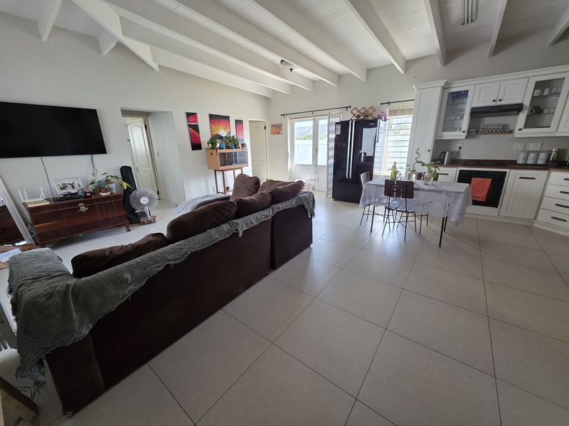 Spacious open-plan living and kitchen area featuring exposed beam ceilings, neutral tiled flooring, and a functional kitchen with built-in cabinetry and integrated appliances.