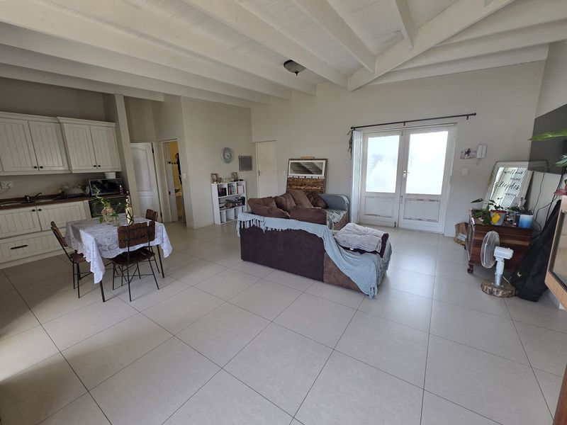 Spacious open-plan living area featuring tiled floors, exposed beam ceilings, and an integrated kitchen with built-in cabinetry, leading to a bright outdoor access point.