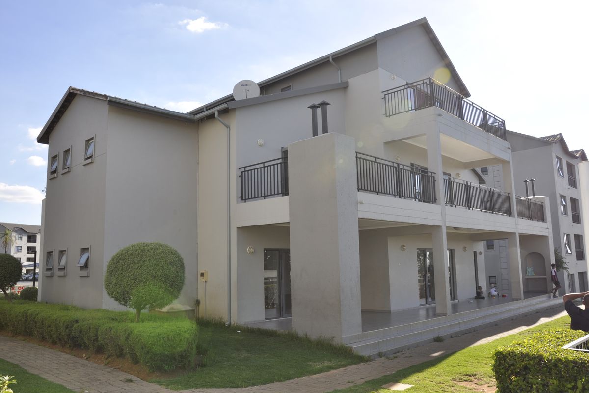 Exterior view of a multi-story apartment building featuring private balconies with metal railings, paved walkways, and well-maintained landscaped garden areas.