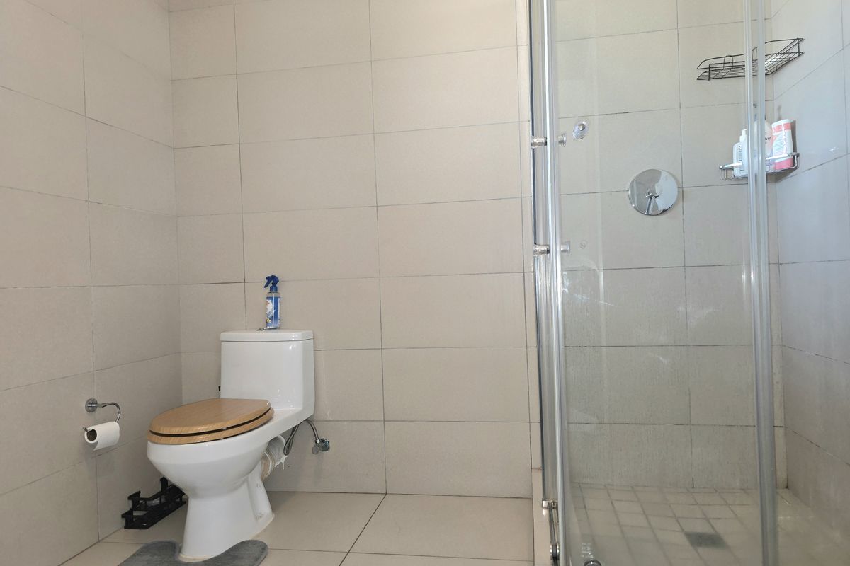 A clean, modern bathroom featuring neutral wall and floor tiles, a white toilet, and a glass-enclosed shower unit.