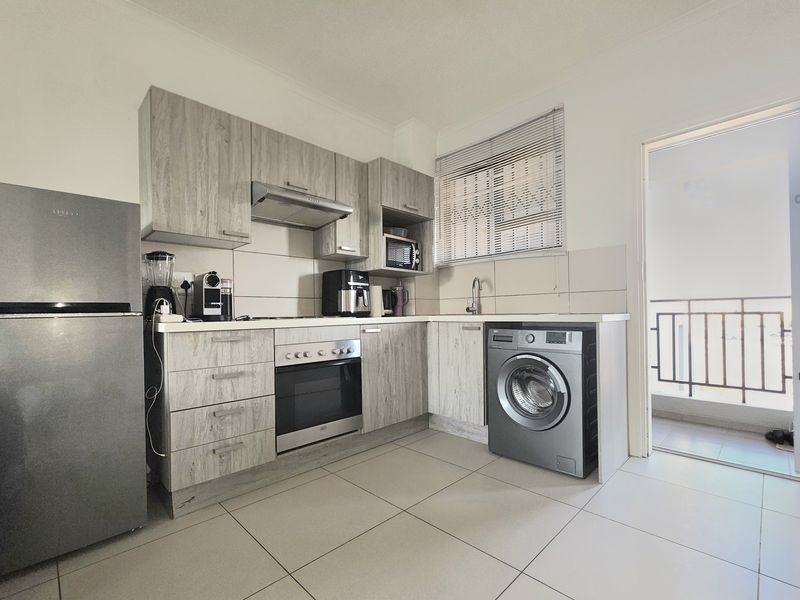A functional kitchen featuring wood-look cabinetry, integrated oven with extractor fan, tiled flooring, and direct access to an outdoor balcony area.