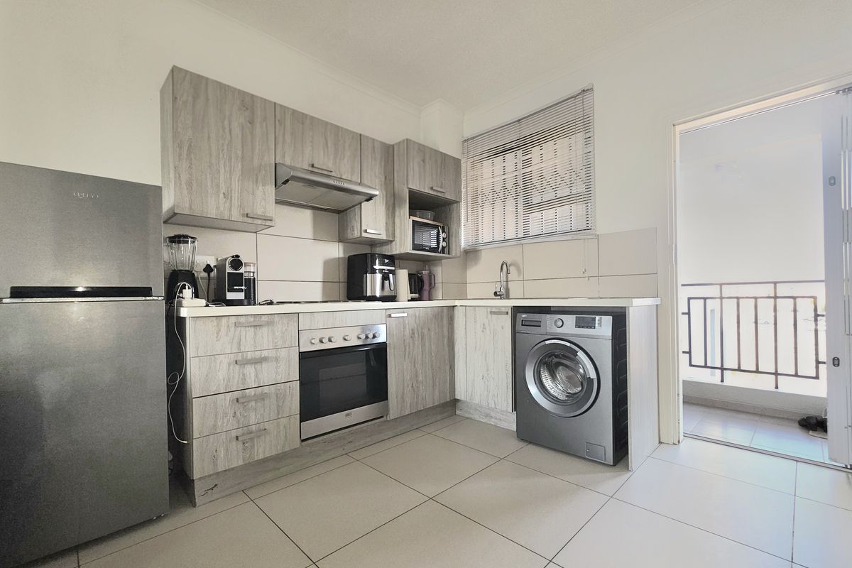 A functional kitchen featuring wood-look cabinetry, integrated oven with extractor fan, tiled flooring, and direct access to an outdoor balcony area.