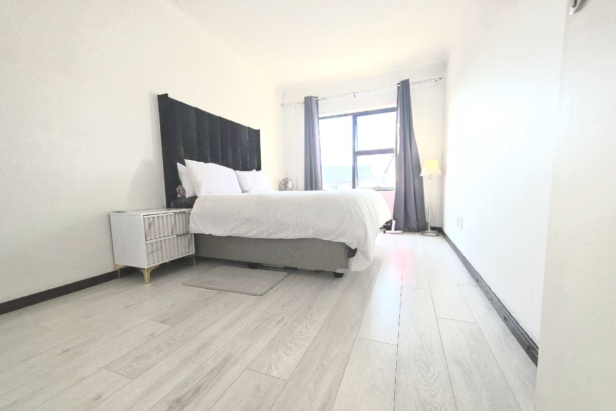 A bright bedroom featuring light-toned laminate flooring and a large window, providing a clean and neutral foundation for personal styling.
