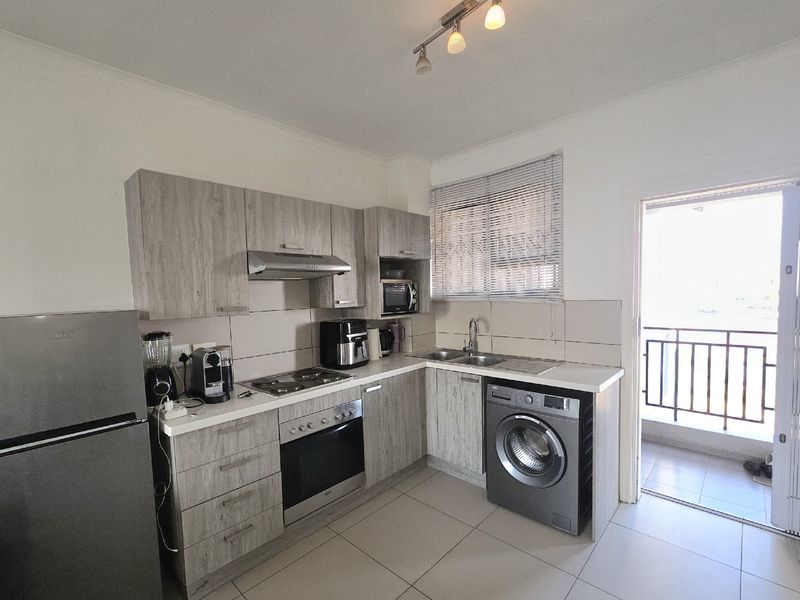 Functional kitchen featuring light wood-grain cabinetry, tiled backsplash, built-in oven and hob, and direct access to an adjoining balcony.