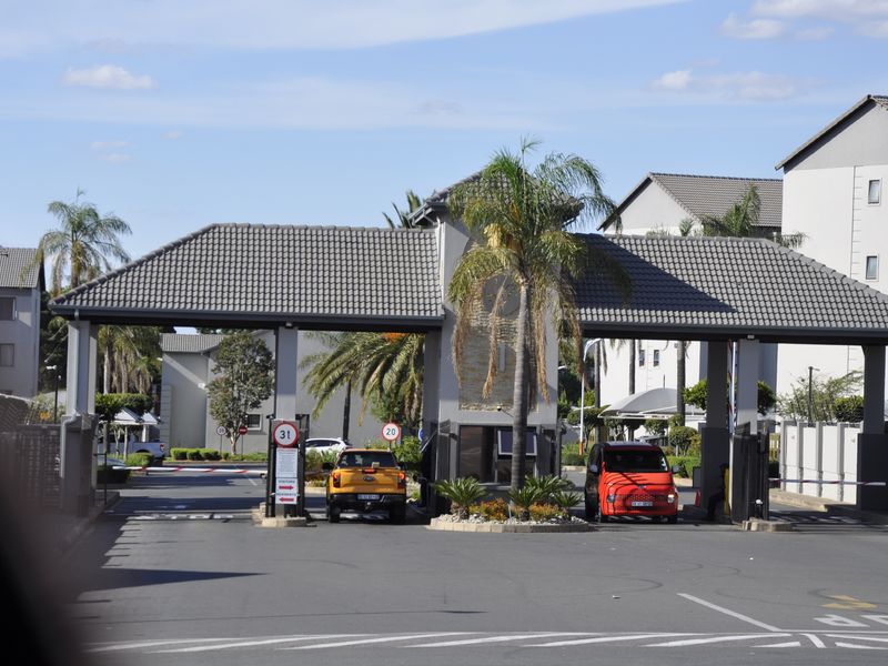 A secure gated entrance to an apartment complex featuring a guardhouse, boom gates, and paved access roads.