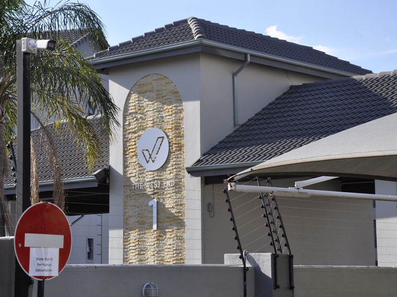 Front facade of The West End apartment complex featuring stone cladding, tiled roofing, and integrated security infrastructure including electric fencing and surveillance.
