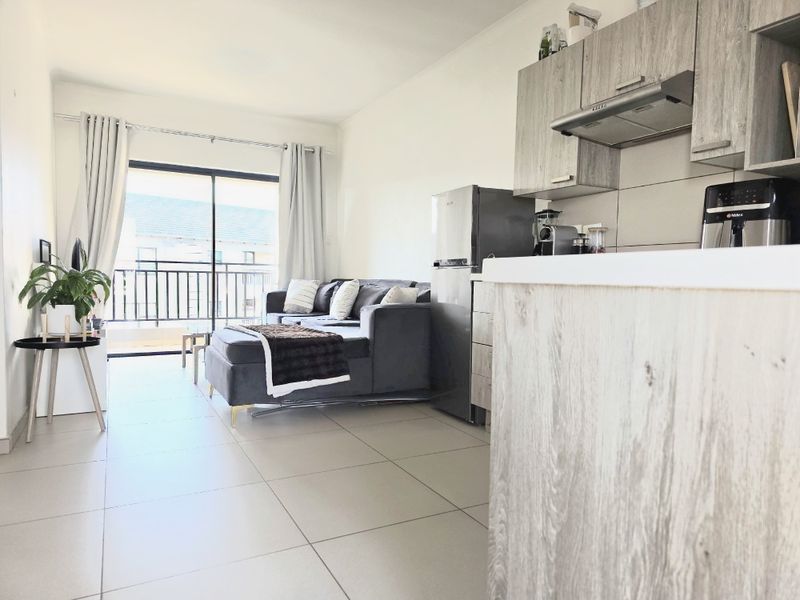 Open-plan living area featuring a modern kitchen with built-in cabinetry and tiled flooring, leading to a balcony through a sliding glass door.