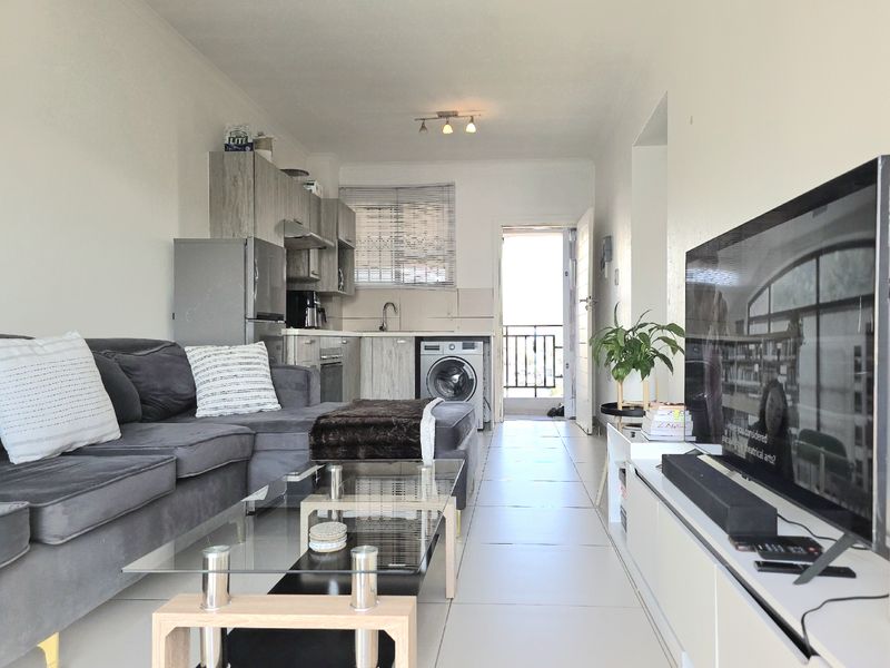 Open-plan living area featuring a compact kitchen with built-in cabinetry, tiled flooring, and direct access to an outdoor balcony.