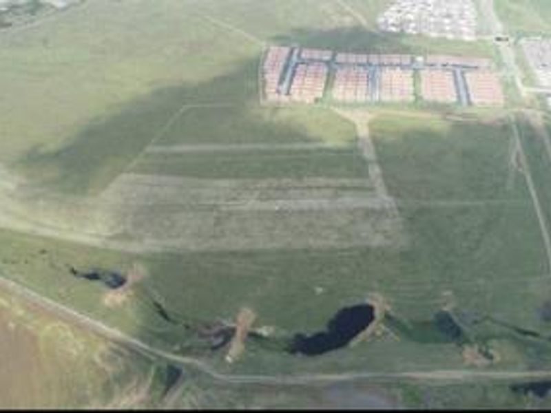 An aerial view of a large, undeveloped residential land parcel featuring open green space and natural drainage areas.