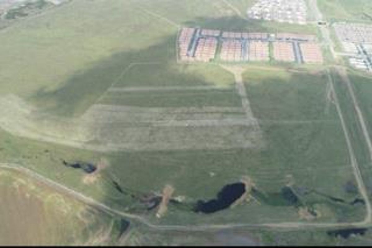 An aerial view of a large, undeveloped residential land parcel featuring open green space and natural drainage areas.