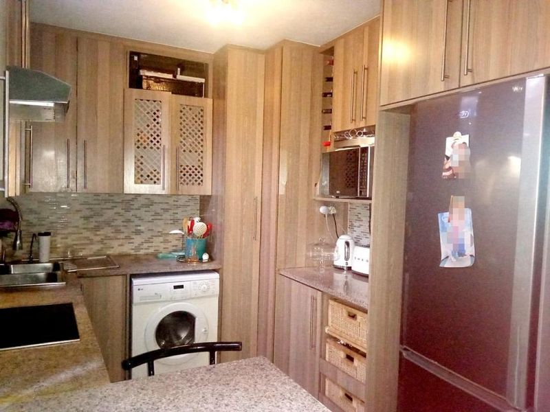 Compact kitchen featuring wood-look laminate cabinetry, granite countertops, mosaic tile backsplash, and integrated appliances including a washing machine and built-in microwave.