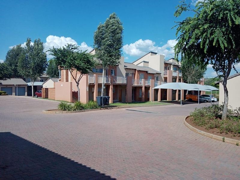 Exterior view of a residential apartment complex featuring paved driveway, covered parking bays, and private balconies.