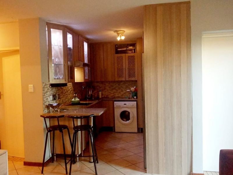 Compact kitchen featuring wood-finish cabinetry, granite countertops, a breakfast bar, and integrated laundry facilities with tiled flooring throughout.