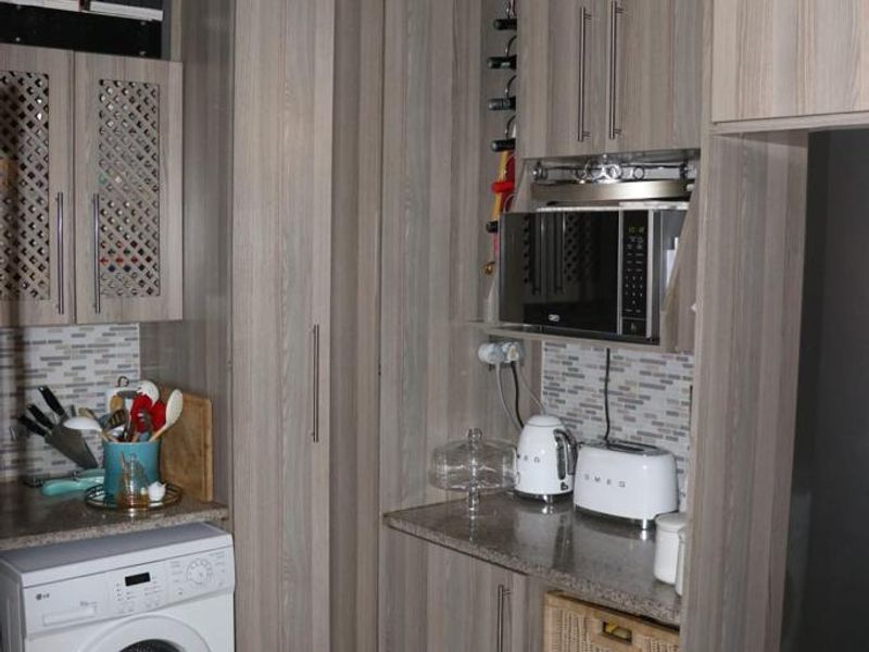 A compact kitchen featuring wood-grain cabinetry, stone countertops, a mosaic tile backsplash, and integrated storage solutions including a built-in microwave and wine rack.