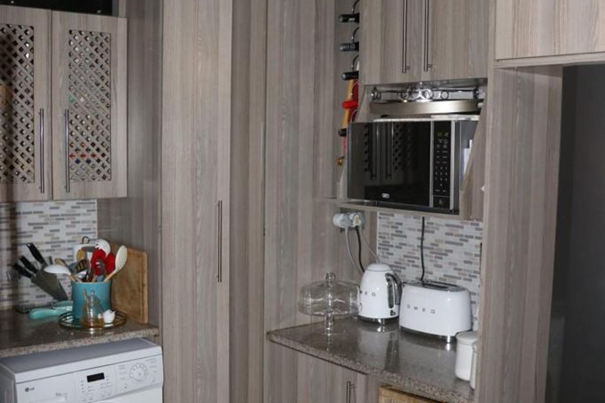 A compact kitchen featuring wood-grain cabinetry, stone countertops, a mosaic tile backsplash, and integrated storage solutions including a built-in microwave and wine rack.