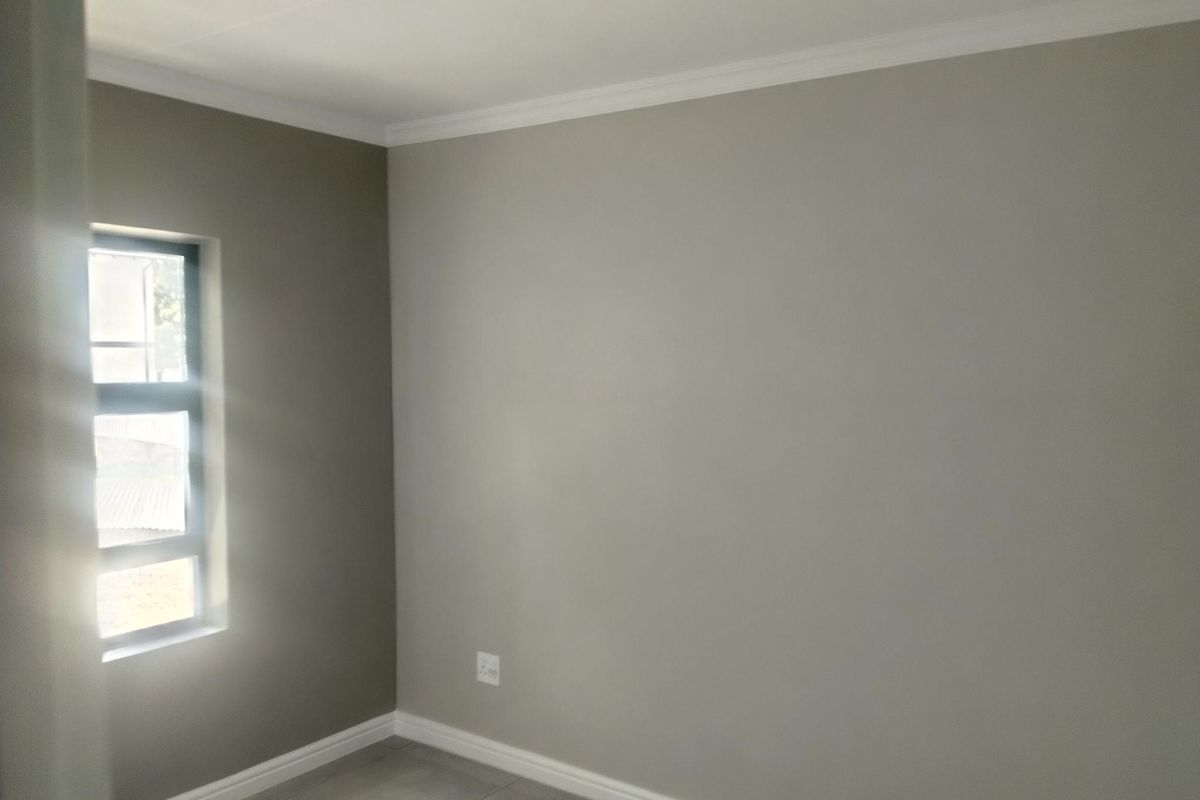 A clean, empty bedroom featuring neutral painted walls, tiled flooring, and a modern aluminium window frame with natural light.
