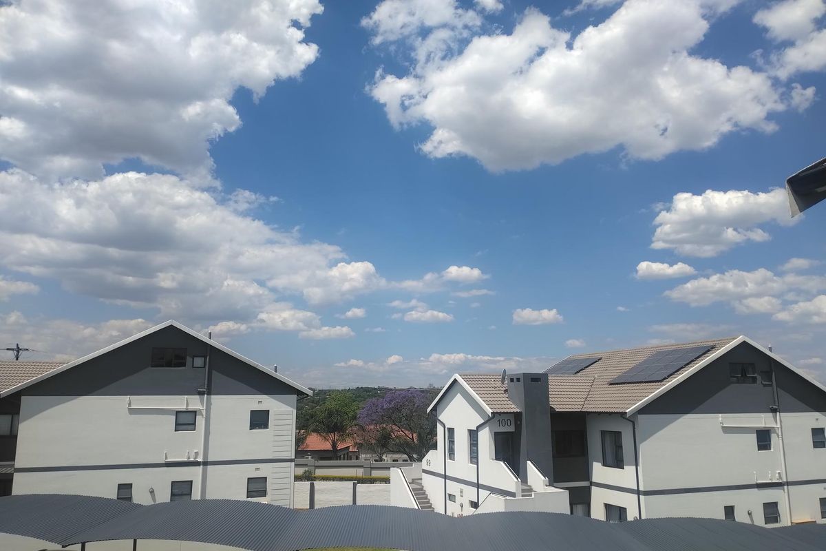 Exterior view of apartment complex buildings featuring modern grey and white facades, tiled roofs with solar panels, and covered parking structures.