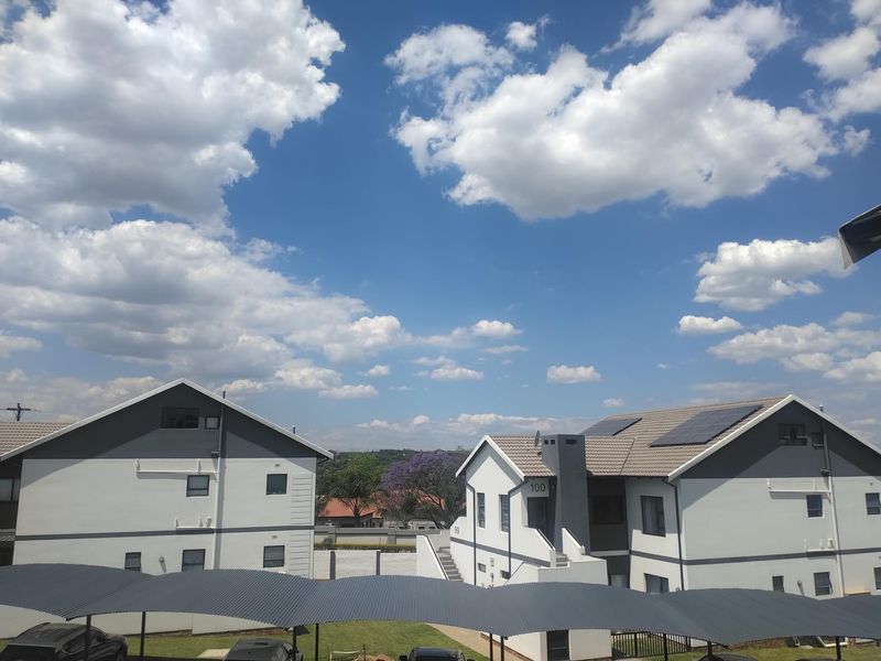 Exterior view of apartment complex buildings featuring modern grey and white facades, tiled roofs with solar panels, and covered parking structures.