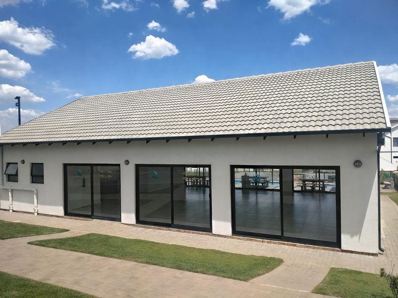 Exterior view of a modern clubhouse building featuring a tiled roof, large sliding glass doors, and a surrounding paved walkway.