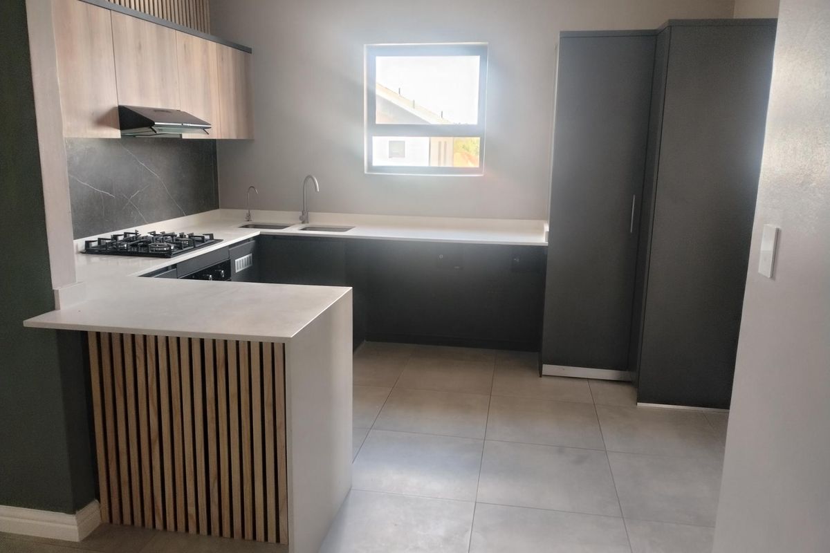 Modern kitchen featuring sleek dark and wood-tone cabinetry, stone countertops, a gas hob with extractor, and high-quality tiled flooring.