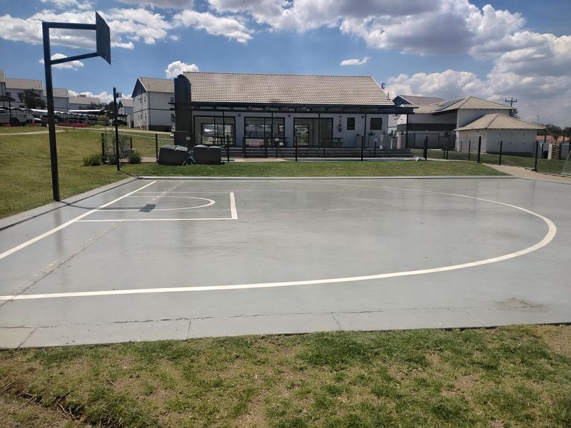 A well-maintained outdoor basketball court featuring a paved surface, hoop, and surrounding lawn area within a residential estate complex.