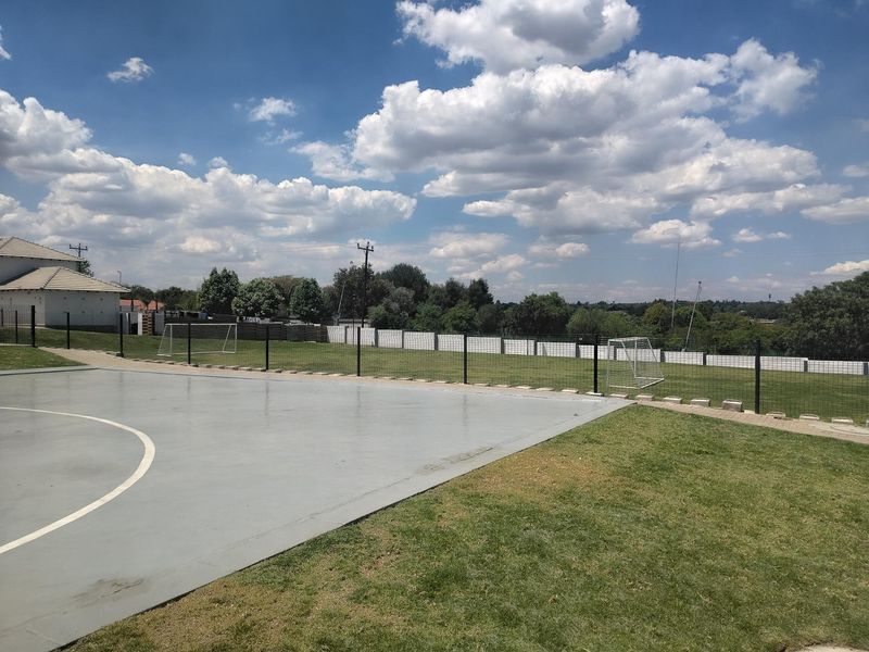 A well-maintained outdoor sports facility featuring a paved court area, grass lawn, and secure perimeter fencing.